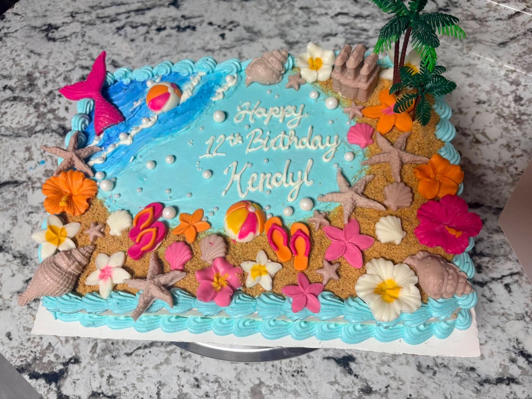 Beach-themed birthday cake with shells, flowers, and ocean details